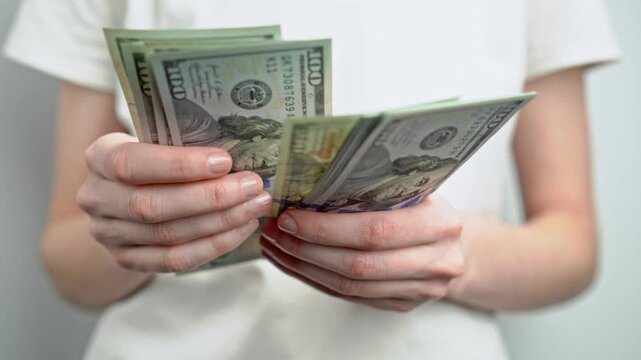 Woman in white t-shirt counting stack of dollar banknotes. Personal finance, cash savings, income, wealth, investment, budgeting and money management concept.	
