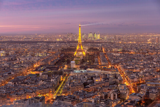 Panoramic view of Paris, France, at sunset with illuminated streets, dense urban architecture.