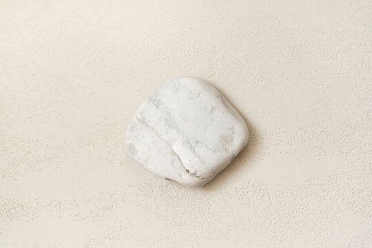 White natural stone with irregular shape and rough surface texture placed in the lower right corner of a clean light neutral background, with open copy space for cosmetic advertising