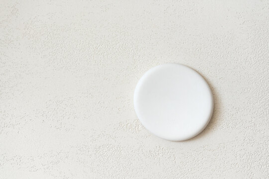 Round flat white stone pedestal placed against a close-up travertine surface in warm beige tones, with open copy space on the left and above for cosmetic advertising and beauty product presentation.