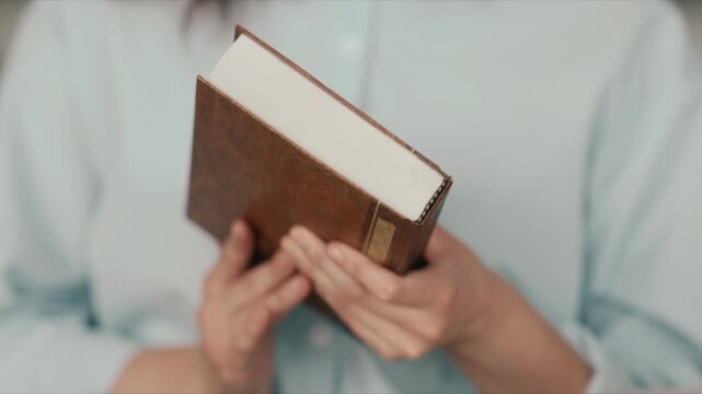 Close up of hands holding open book reading intently in soft light wearing white shirt