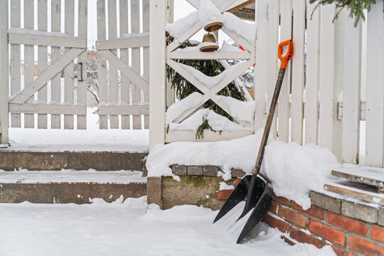 Snow covered porch with shovel and snowblower during a winter storm. Residential property maintenance, seasonal snowfall