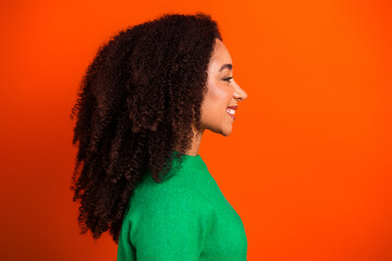 Smiling woman in green sweater profile portrait against bright orange background conveying confidence and joy © deagreez