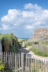 Fototapeta premium A sandy path leading to the sea between wooden fences and an old concrete WWII military bunker on a coastal sand dune at Juno Beach.