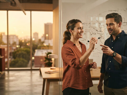 Woman and man discussing handwritten workflows on a whiteboard beside a sunset office window