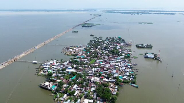 Aerial view of a flooded village surrounded by water with a long causeway connecting to the mainland in Kishoreganj, Dhaka Division, Bangladesh.