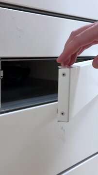 A hand opens a white metal parcel locker to retrieve an order, illustrating modern logistics, contactless pickup service, and efficient automated delivery box technology Vertical