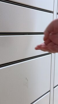 A hand opening a white metal storage locker door to reveal a compartment, illustrating secure parcel delivery or automated storage service in a modern logistics environment Vertical