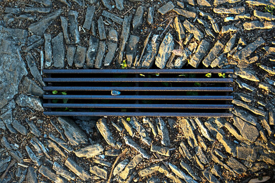 Rusty metal drain grate surrounded by rough stone paving