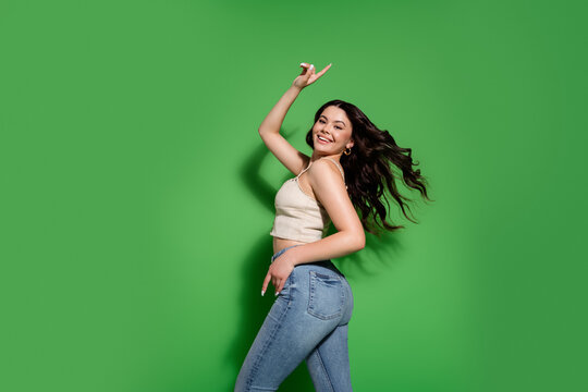 Young smiling woman dancing in jeans and a crop top against a bright green background expressing joy and confident casual style