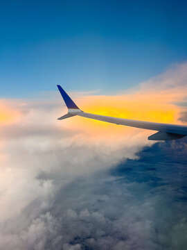 Vertical shot of airplane wing in the sky over clouds at sunset or sunrise