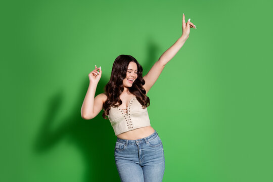 Young woman dancing and smiling in casual crop top and jeans against a green studio background, carefree joyful lifestyle portrait