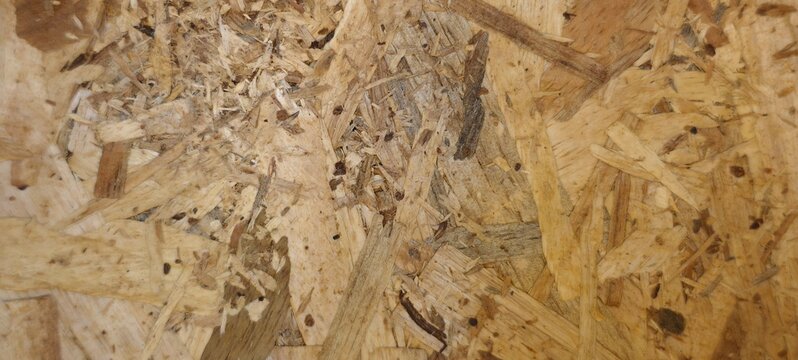 Detailed view of oriented strand board (OSB) showing compressed layers of irregular wood flakes in shades of brown and beige. 