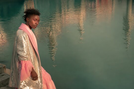 Fashion model in silver sequin coat by calm water in soft pink evening light