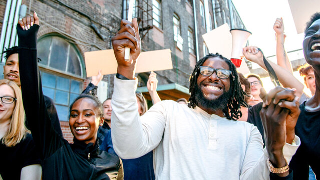 Diverse group of people cheer and hold signs during an outdoor protest or rally.