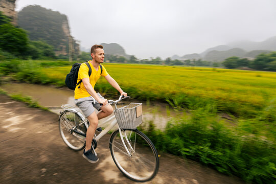 Tourist riding bicycle on road between rice fields with limestone karst mountains background in Ninh Binh Vietnam. Eco tourism, outdoor cycling adventure and rural Asian travel concept.