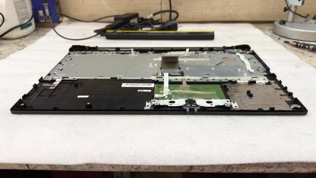 A disassembled laptop case with circuit board and ribbon cables lies on a workbench. Computer repair, spare parts, device service, PC electronics