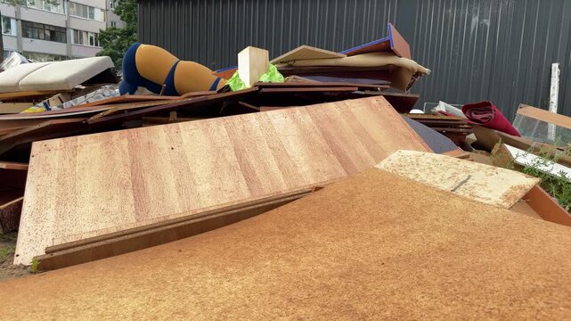 A pile of broken furniture, wooden boards and old sofa parts lies near a metal fence. Bulky waste, furniture disposal, household junk, home cleanup