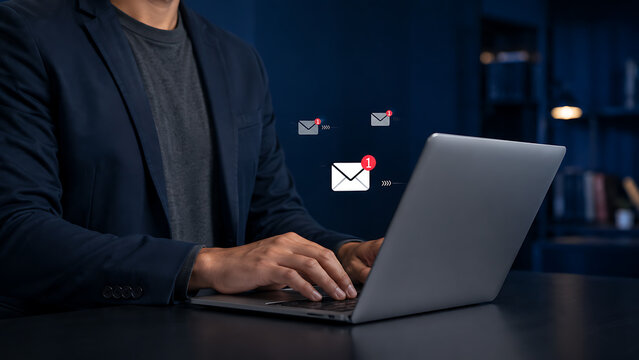 Professional businessman working on laptop receiving unread email notifications with red badge counter icon in dark modern office workplace setting during evening