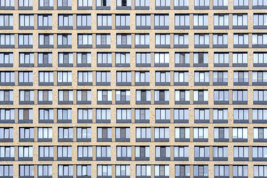 Yellow brick skyscraper facade with symmetrical glass windows grid. Repetitive modular pattern of modern residential apartment building exterior.