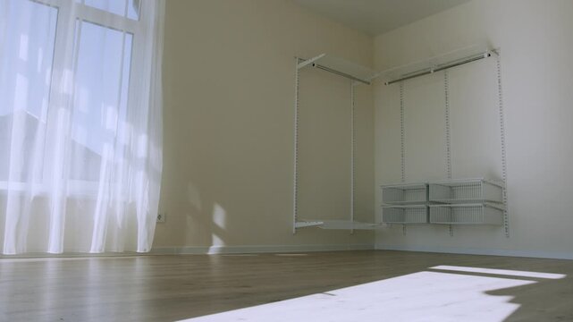Empty room in a modern country house with wooden floor, white walls, large window and open shelving unit. Bright minimalist residential interior with natural daylight.
