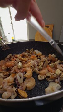 Hand Stirring Mixed Seafood in a Black Pan, Close Kitchen View of Home Food Preparation, Healthy Eating and Fresh Cooking Slow motion Vertical video.