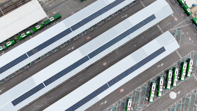 Aerial view of electric buses parked at a charging depot with solar panels on the roof structures in Milan, Lombardy, Italy.
