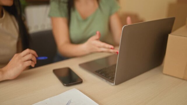 Woman hands typing on laptop and pointing at smartphone and parcel on desk in office building; teamwork focus productivity.