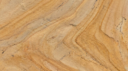 Obraz premium Close-up of textured sandstone surface exhibiting natural swirling patterns and warm earthy hues for detailed geological or