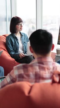 A group of young professionals in casual attire are engaged in a video conference call while relaxing on beanbag chairs in a modern office space
