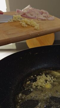 Chopped Garlic Falls into Melted Butter in a Black Frying Pan, with Sliced Shallot on a Wooden Board, Showing Fresh Food Preparation Slow motion Vertical video. Vertical video.