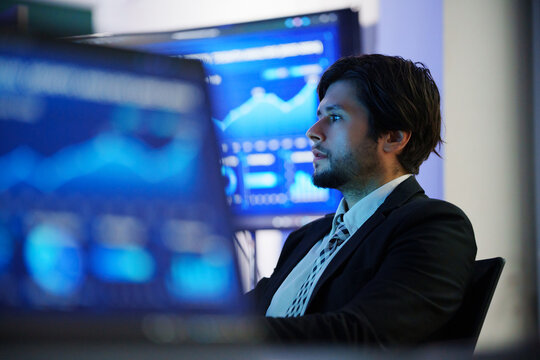 Business analyst monitoring data dashboards on multiple screens in a technology office, representing cybersecurity, network security, data analysis, AI systems and digital performance monitoring.