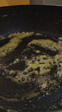 Minced Garlic Sizzles in Melted Butter, Stirred With a Metal Spatula in a Black Skillet, Close Up Food Preparation Showing Fresh Aromatic Cooking Slow motion Vertical video. Vertical video.