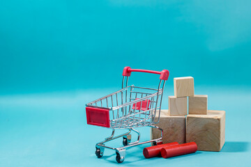 Horizontal composition featuring an empty mini shopping cart with wooden blocks on a vibrant blue surface. High Quality Photo © 7TridentSea