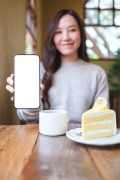 Vertical mockup image of a woman holding and showing a mobile phone with blank white screen in cafe