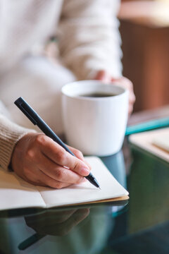 Vertical closeup image of a woman writing on a notebook on the table