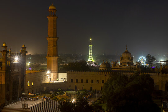 View of the illuminated Badshahi Mosque at night with its towering minarets and domes, set against the city skyline of Lahore, Punjab, Pakistan.