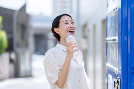 自販機で飲み物を買って飲む女性