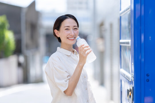 自販機で飲み物を買って飲む女性