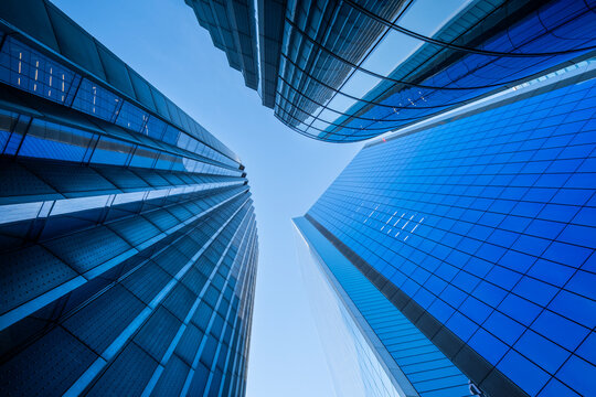 A wide perspective opens on sky in London's financial district, while glass planes pull the view upward and office architecture narrows around a skyscraper facade.