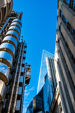 Exposed steel frames an upward office view, while architecture in London, England, surrounds an industrial tower in the financial district, its facade against sky.