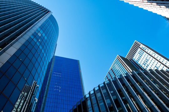 A low perspective opens on sky in London, England, while glass walls in the financial district shape a skyscraper beside curved office architecture and its facade.