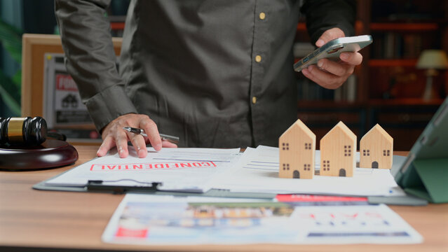 Lawyer reviewing property contract documents beside house models gavel holding smartphone consultation legal agreement office desk transaction market.
