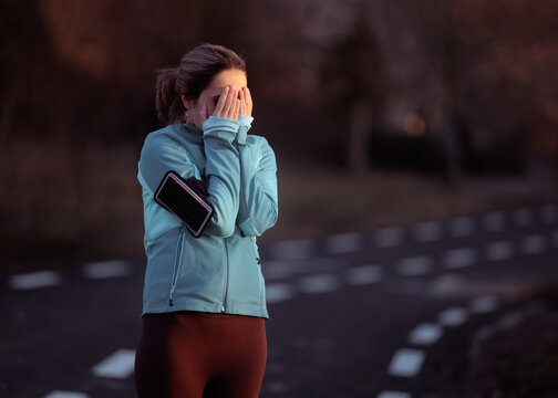Exhausted Female Runner Covering Her Face During Outdoor Workout. Tired young woman in sportswear crying or hiding face on park path