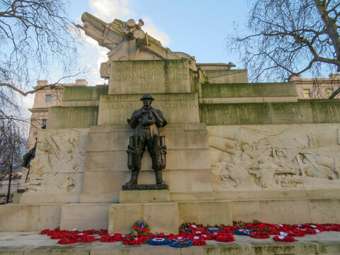 View of the Royal Artillery Memorial featuring a bronze soldier statue, stone carvings, and an artillery piece, with poppy wreaths at the base in London, England, United Kingdom.