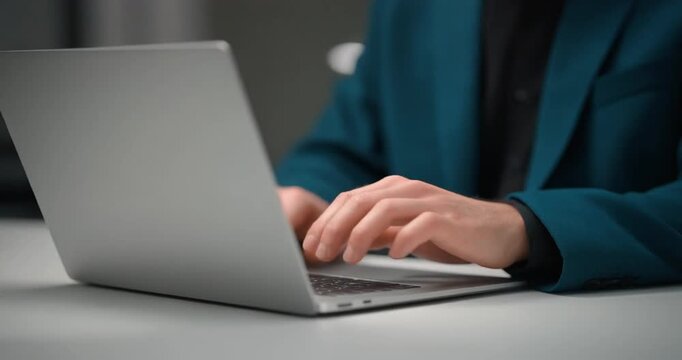 Businessman in teal blazer typing on a laptop keyboard in a professional office setting.