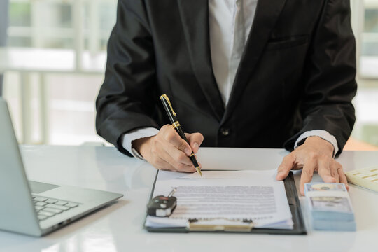 Businessman Signing Car Loan or Vehicle Insurance Contract with Money and Key on Desk