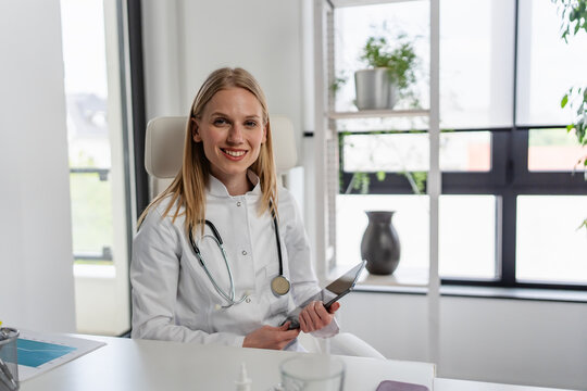 Approachable female physician smiling warmly from her desk, representing a trusted family doctor and personalized primary healthcare