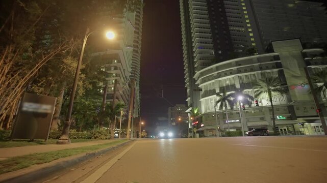Miami urban street scene at night featuring tall buildings and glowing car headlights