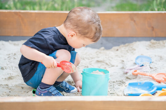 Curious child exploring sand with colorful toys during outdoor playtime.